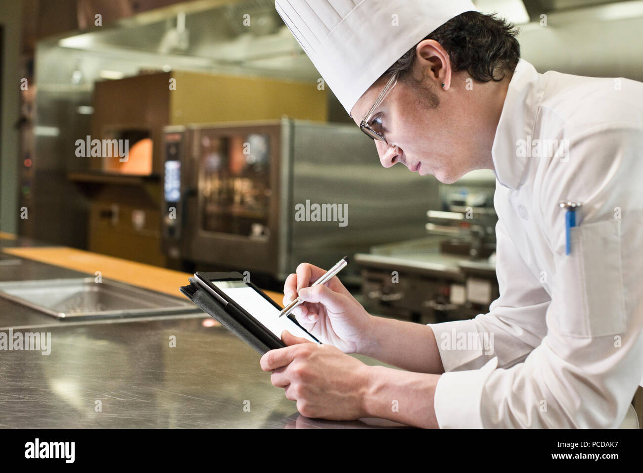 Ein Kaukasier Männlich Chef arbeiten auf ein Notebook in einer gewerblichen Küche. Stockfoto