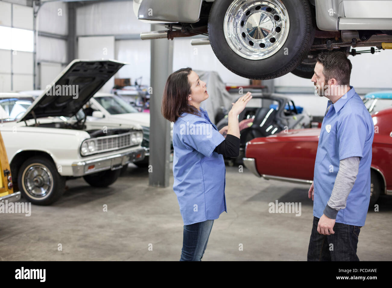 Zwei europäische männlich und weiblich Kfz-Mechaniker bei der Arbeit auf ein Auto in ein klassisches Auto Reparaturwerkstatt. Stockfoto
