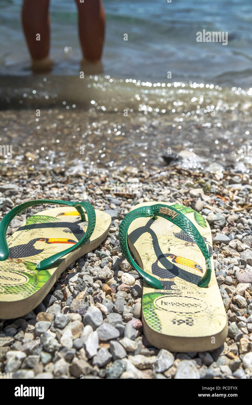 Flip Flops am Ufer des Lago di Ledro, während die Eigentümer ein erfrischendes Bad im See nehmen. Stockfoto