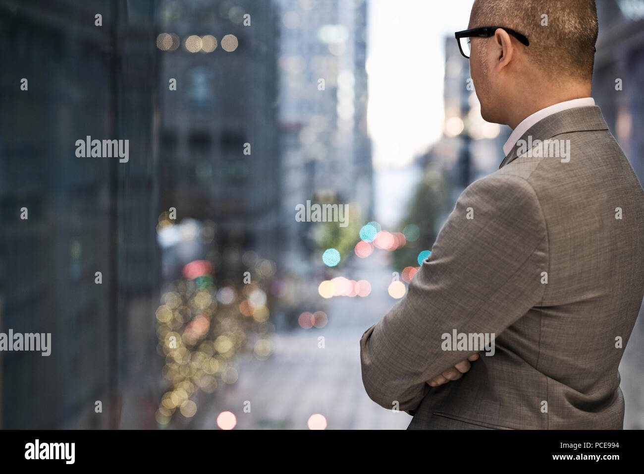 Ein Blick von hinten ein Geschäftsmann, der an ein Fenster an einer Stadt street scene Suchen beleuchtet kurz vor Einbruch der Dunkelheit. Stockfoto