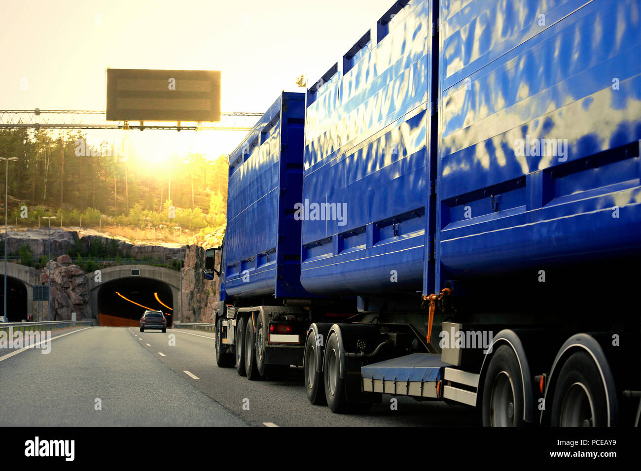 Blau Heavy Transport-LKW fährt auf der Autobahn unter Verkehr in Richtung eines Straßentunnels und Sonnenuntergang am Abend. Stockfoto