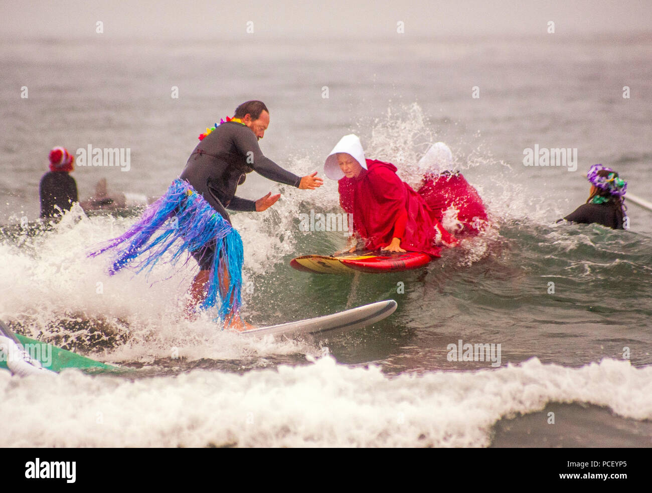 In den Kostümen von' die Geschichte der Dienerin", zwei Surfer kaum verpassen eine andere sporting ist ein Hula-tänzerin gras Rock zu einem Halloween kostümiert surfen Ereignis in Huntington Beach, CA. (Foto von Spencer Grant) Stockfoto