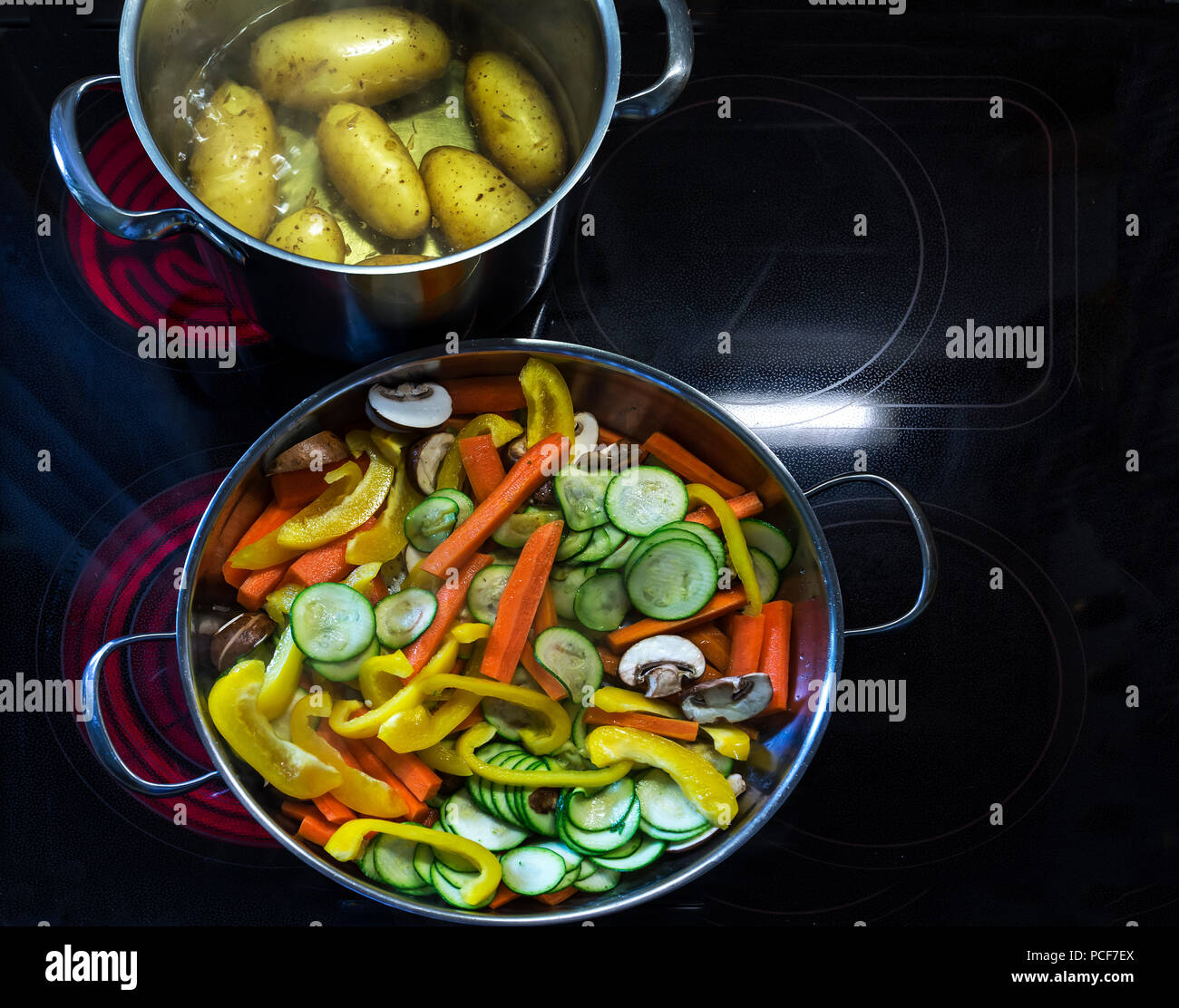 Frisch geschnittenes Gemüse, Karotten, Paprika, Champignons und Auberginen in einer Pfanne und kochende Kartoffeln rot, Kochplatten, Deutschland Stockfoto