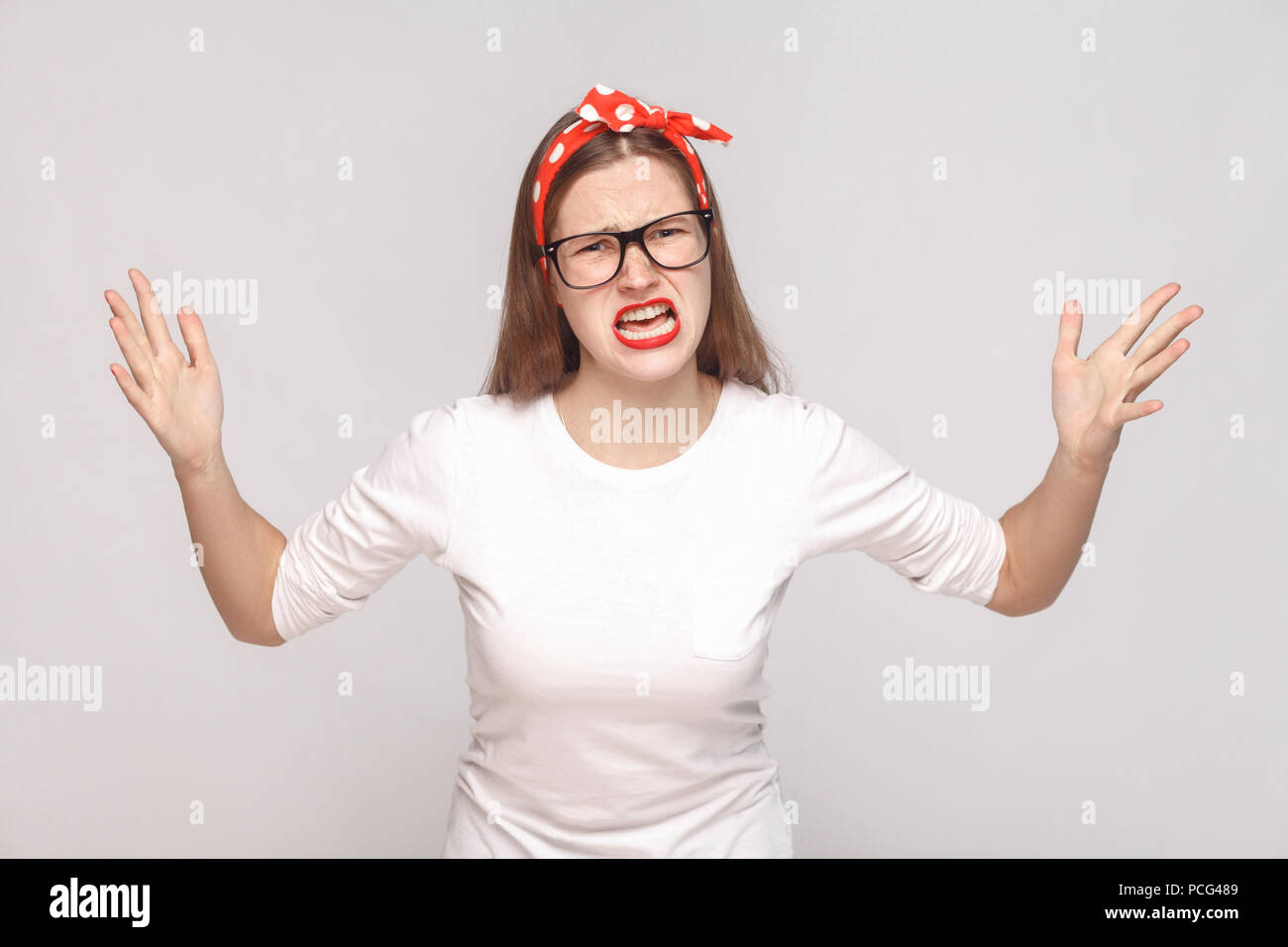 Was wollen Sie? Portrait von unzufriedenen wütend emotionale junge Frau im weißen T-Shirt mit Sommersprossen, schwarze Brille, rote Lippen und Kopfband. indoor St Stockfoto