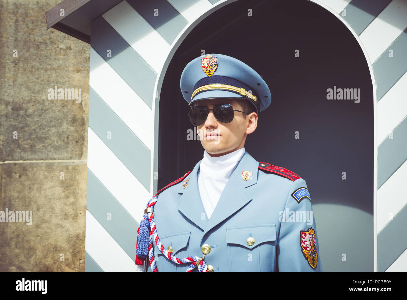 Ein junger Mann in der Sonnenbrille, Sommer Uniform und Mütze steht außerhalb der Prager Burg Tore und gestreifte Schaltschrank auf Pflicht als Teil der Schutzeinrichtung. Der Tschechischen Republik. Stockfoto