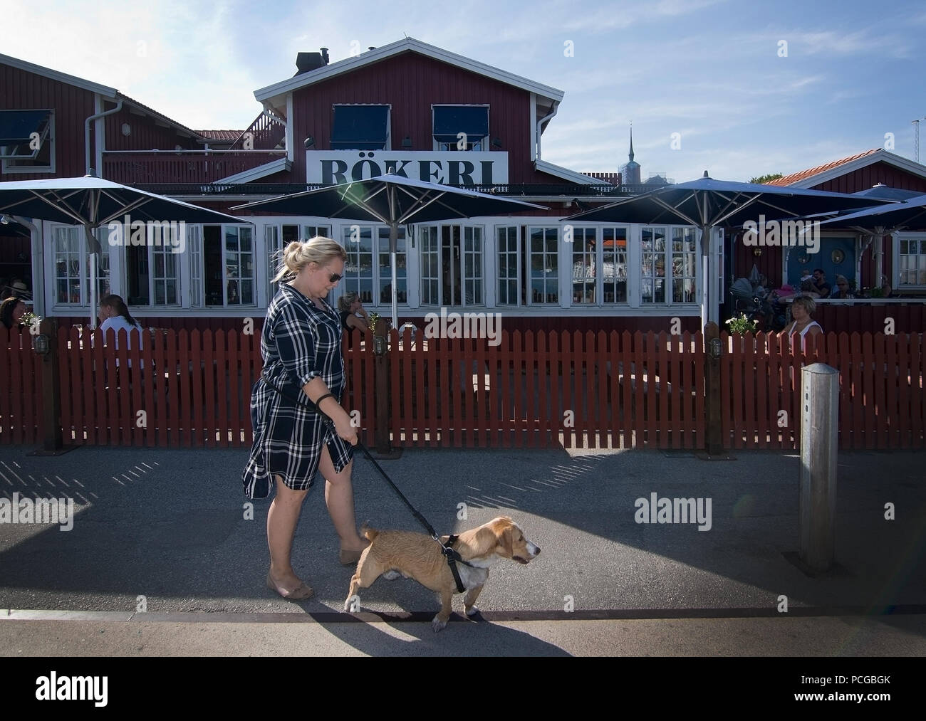 NYNASHAMN, Schweden - 18. JULI 2018: Frau geht Hund draußen Nynas rokeri Meeresfrüchte Geschäfte und Läden außen am 18. Juli 2018 in Nynashamn, Schweden. Stockfoto