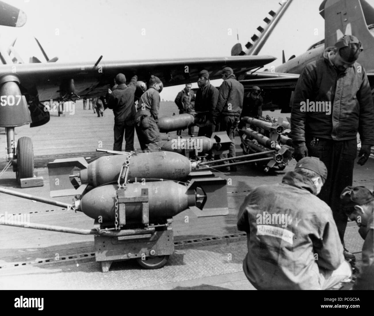 USS philippinischen Meer (CV-47): 250-Pfund Bomben unter den Flügeln eines Douglas AD Skyraider von Attack Squadron 65 geladen werden, während der weg von der koreanischen Küste, 21. Mai 1951. Ein Warenkorb 5-Zoll-Raketen und einen zweiten Wagen mit 250-Pfund Bomben sind ebenfalls vorhanden. Stockfoto