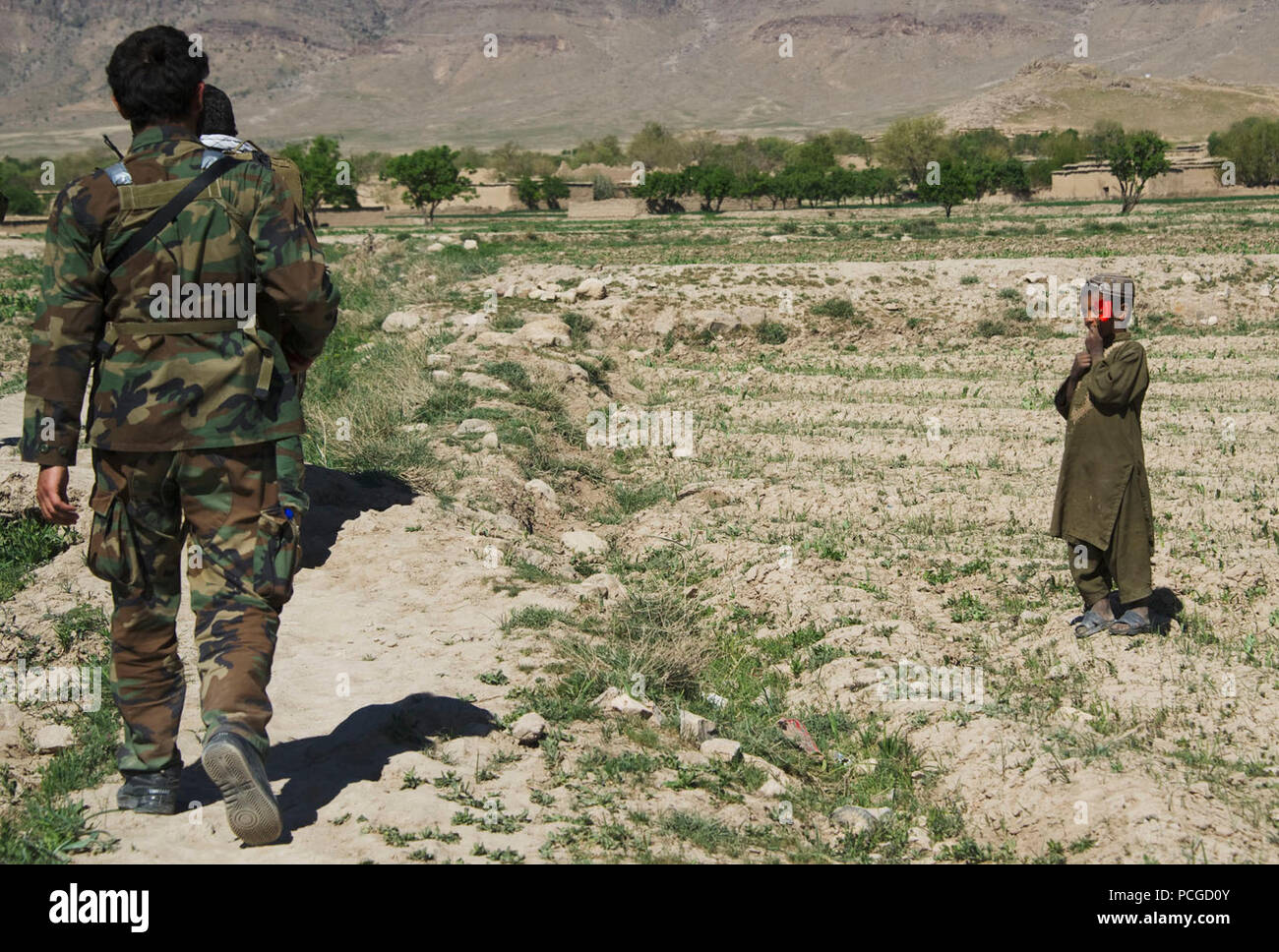 Afghan National Army Special forces Soldaten pass ein junger Dorfbewohner auf dem Weg mit Dorfältesten über den Bau einer Wasser Kanal für Tagaw Bezirk zu sprechen, der Provinz Uruzgan, Afghanistan, am 13. April. Der Kanal wird dafür sorgen, dass Wasser im Sommer gesammelt wird länger dauern und mehr Wasser zur Bewässerung zur Verfügung im Sommer fährt. Stockfoto