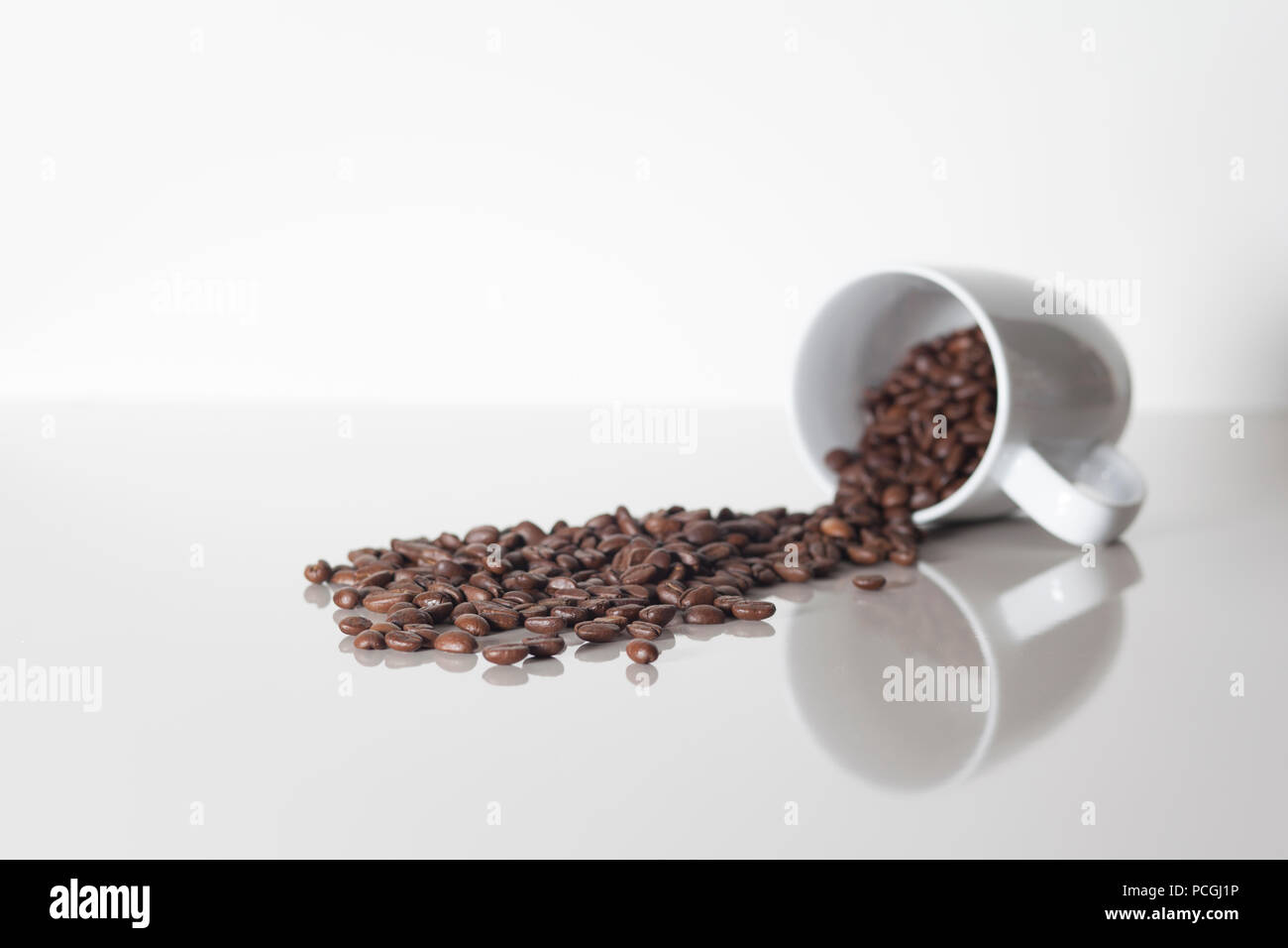 Viele Kaffee Kaffee Bohnen verschütten aus einer Schale auf einem weißen Counterspace mit textspace und eine Reflexion Stockfoto