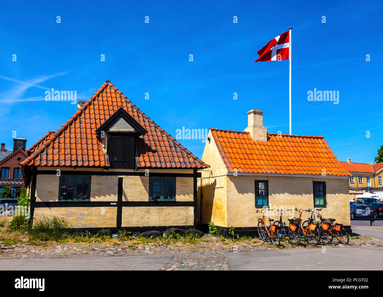 Dänische Flagge; Fliegen; Informationen; Dragør Fischerdorf; Kopenhagen; Dänemark; traditionelle Gebäude; roten Fliesen; Fahrräder; Fahrräder; blauer Himmel Stockfoto