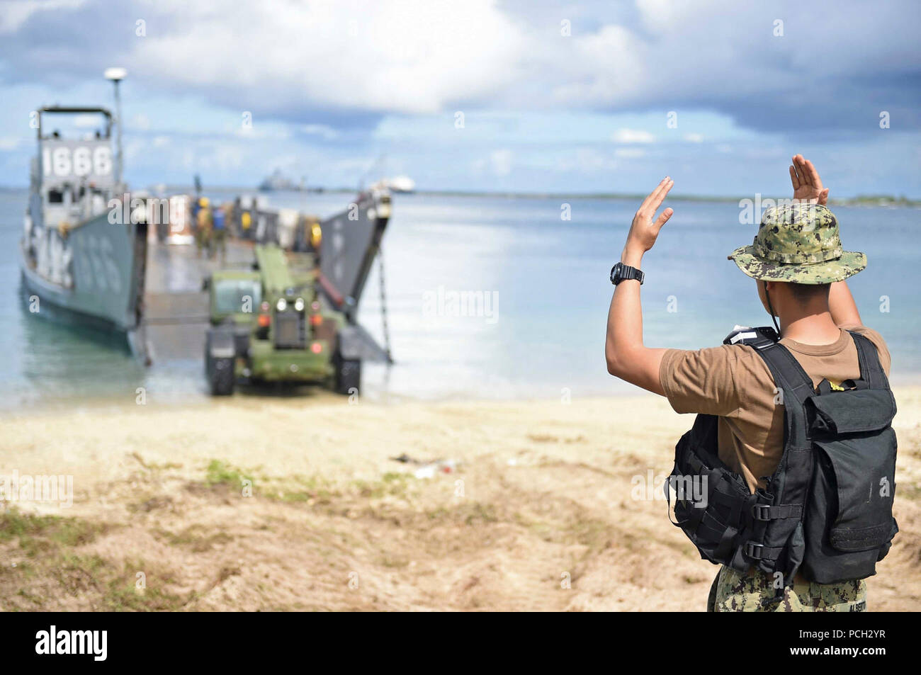 Finden HANDWERK STRAND, Guam (Aug. 10, 2015) von Gunner Mate 3. Klasse Jay Alberto Signale an einen Traktor vor 13.00 Landing Craft Utility (LCU) 1666, zugeordnet zu den Naval Beach (NBU) 7, für Lieferungen von Maschinen und Anlagen zur Katastrophenhilfe in Saipan in die gut Deck des Amphibischen dock Landung Schiff USS Ashland (LSD 48) nach dem Taifun Soudelor geladen werden kann. Stockfoto