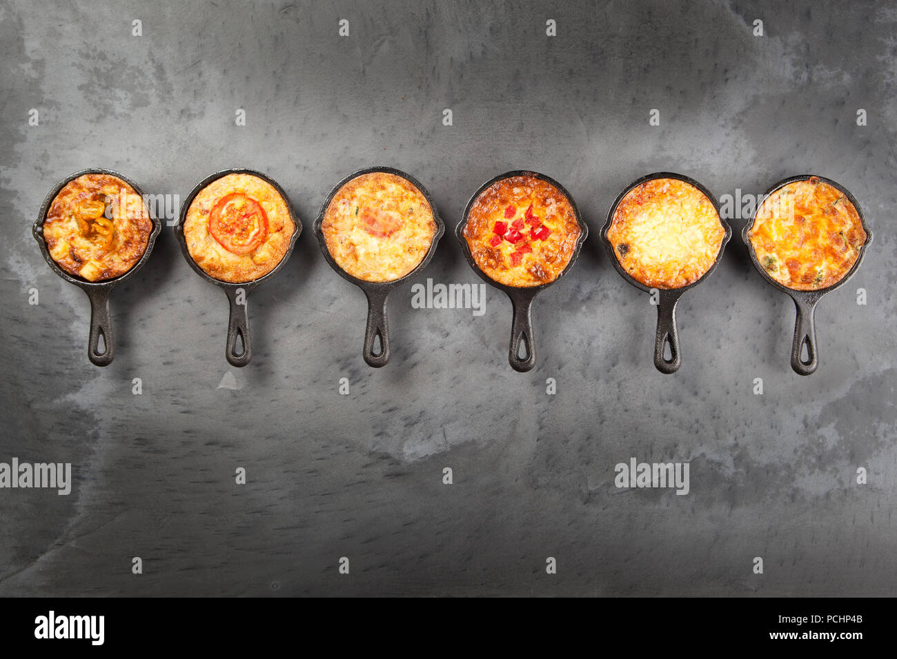 Sechs einzelnen Mini Quiche Torten in Gusseisen Pfannen auf dunklem Schiefer Oberfläche Stockfoto