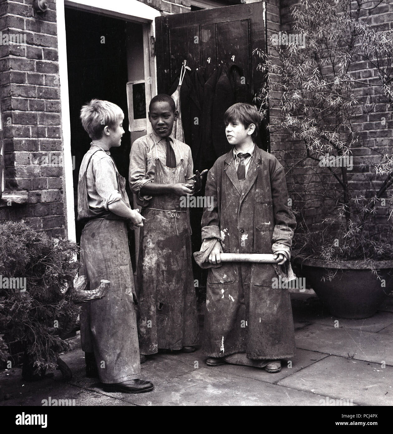 1968, historische, drei junge Schüler tragen Lehm bedeckt Overalls chatten außerhalb ihrer Fertigkeit oder Kunst Workshop, wo Sie Keramik, London, England, UK wurde. Stockfoto