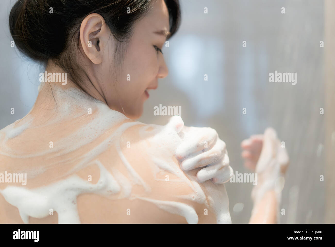 Junge asiatische Frau unter der Dusche im Badezimmer mit Dusche. Suchen glücklich und entspannen. Stockfoto