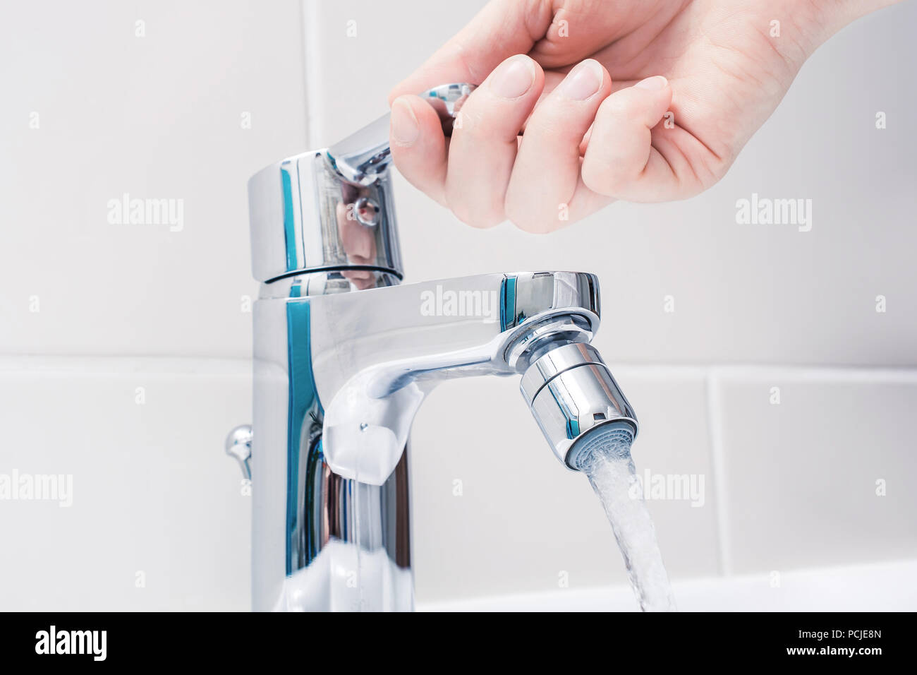 Weibliche Hand auf den Griff eines Chrom Wasserhahn mit fließendem Wasser Stockfoto