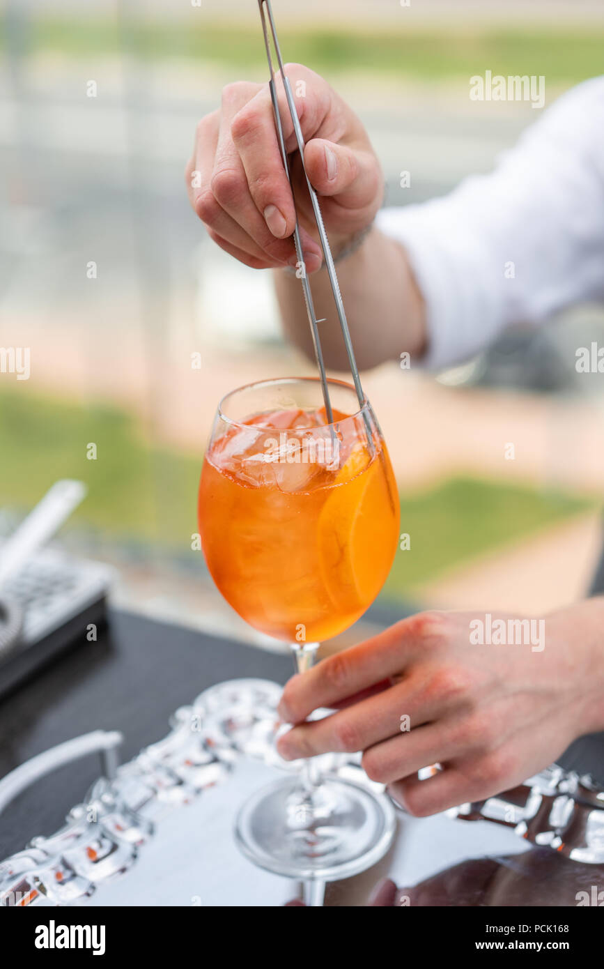 Der Barkeeper macht cocktail Aperol Spritz. Glas, selektiven Fokus besprühen. Alkoholische Getränk auf Theke mit Eiswürfeln und Orangen. Party im Freien Stockfoto