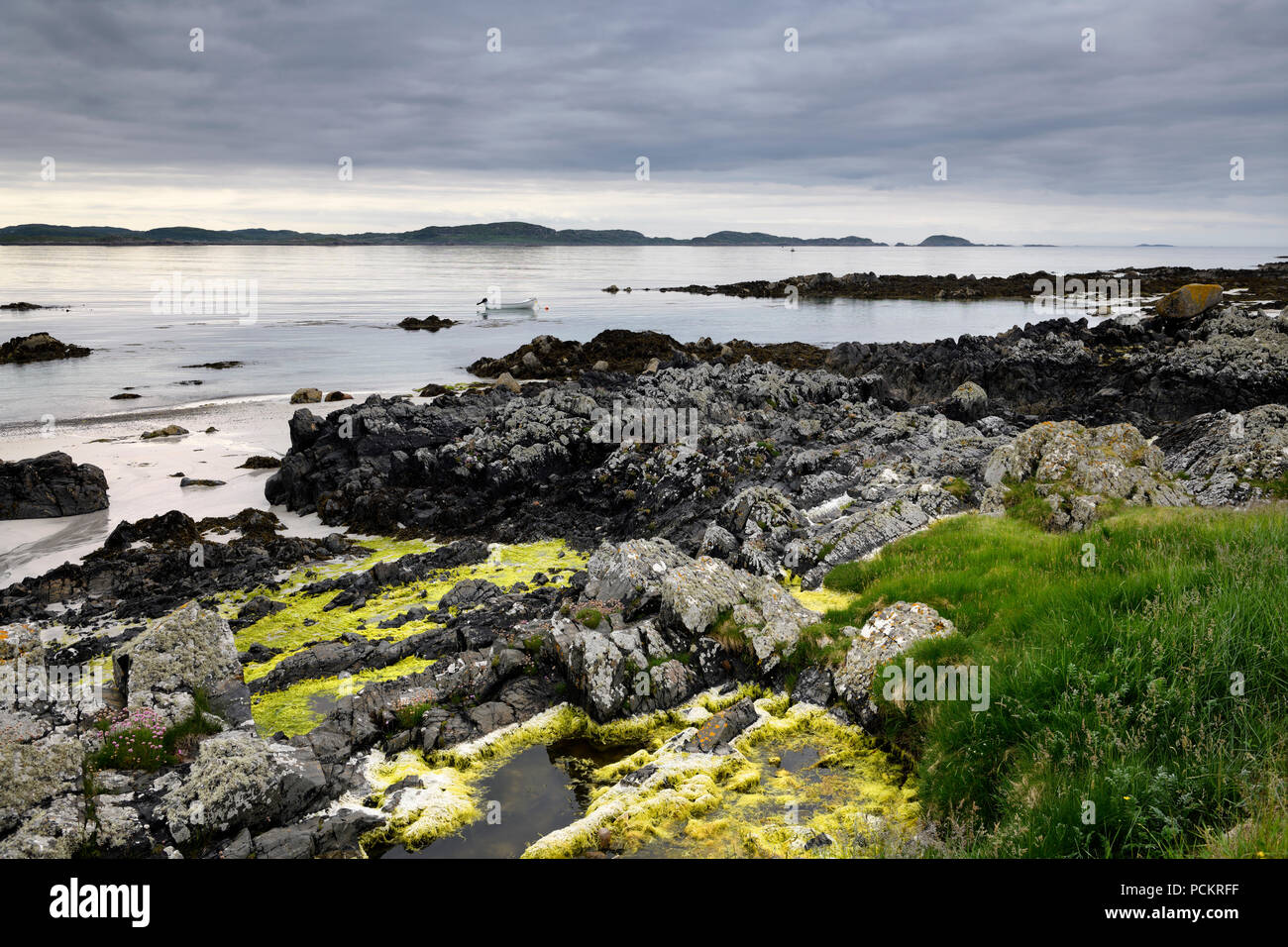 Sandstrand und felsigen Ufer mit Gras und Algen auf der Insel Iona mit Boot auf Sound of Iona Inneren Hebriden Schottland Großbritannien Stockfoto