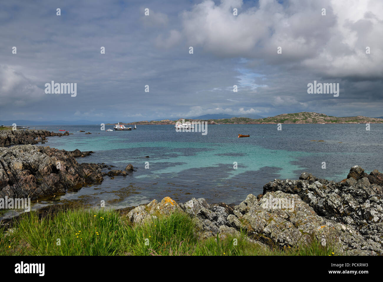 Felsige Küste der Isle of Iona in Isle of Mull und Berge von Ben Mehr und Ausflugsschiffe im Sound von Iona Inneren Hebriden Schottland Großbritannien suchen Stockfoto