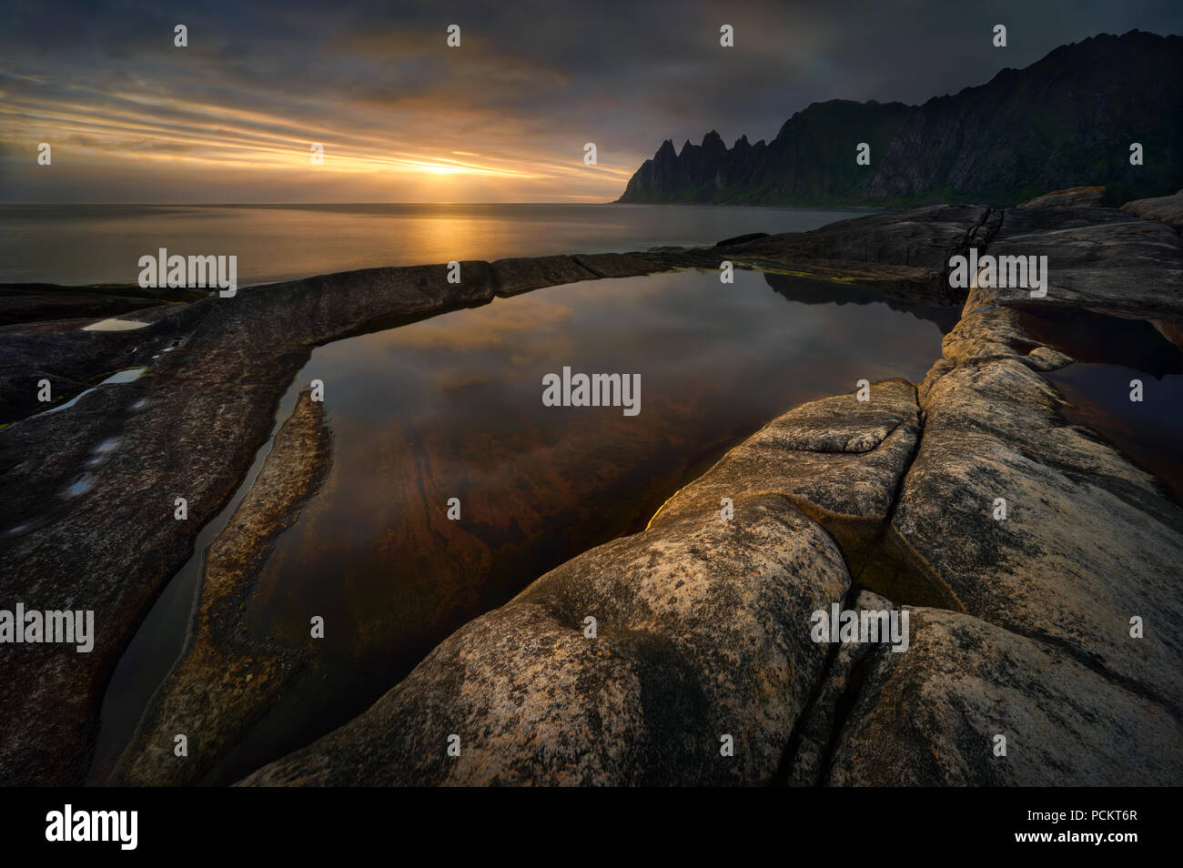 Tugeneset felsige Küste mit Bergen im Hintergrund bei Sonnenuntergang, Senja, Norwegen Stockfoto