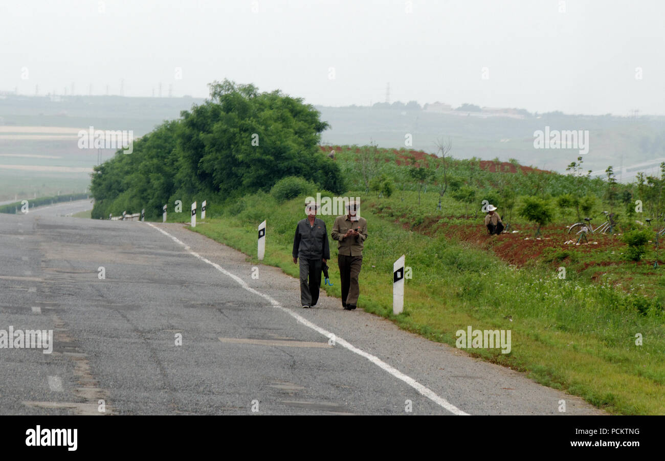 Zwei Nordkoreanische Arbeiter in Licht Uniformen entlang eine einsame leere Straße auf dem Pannenstreifen Radweg in der Landschaft von Nordkoreanischen Stockfoto