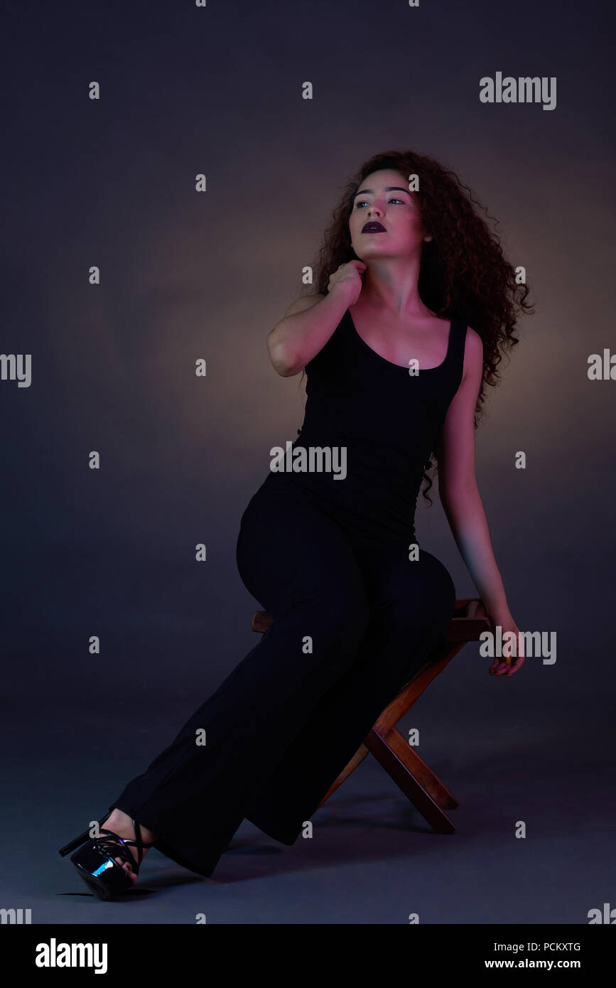 Junge Frau Modell sitzen auf kleinen Stuhl im Studio dunklen Hintergrund Stockfoto