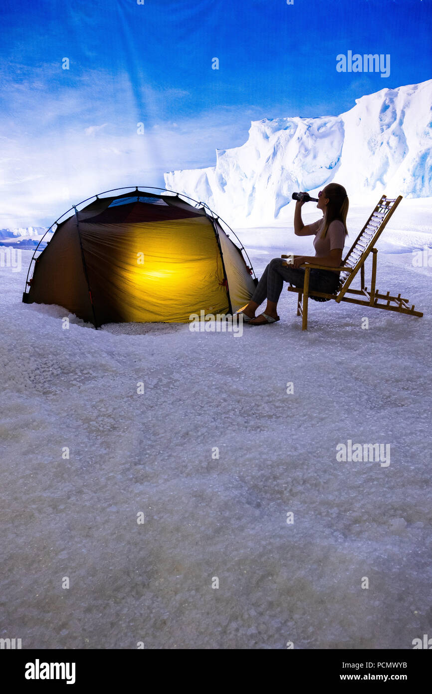 Bremerhaven, Deutschland. 03 Aug, 2018. Ein Mitarbeiter des Klimahauses  Bremerhaven sitzt im Sommer Kleidung auf einem Klappstuhl vor einem Zelt  bei minus sechs Grad in der Antarktis Ausstellung und Getränke aus einer