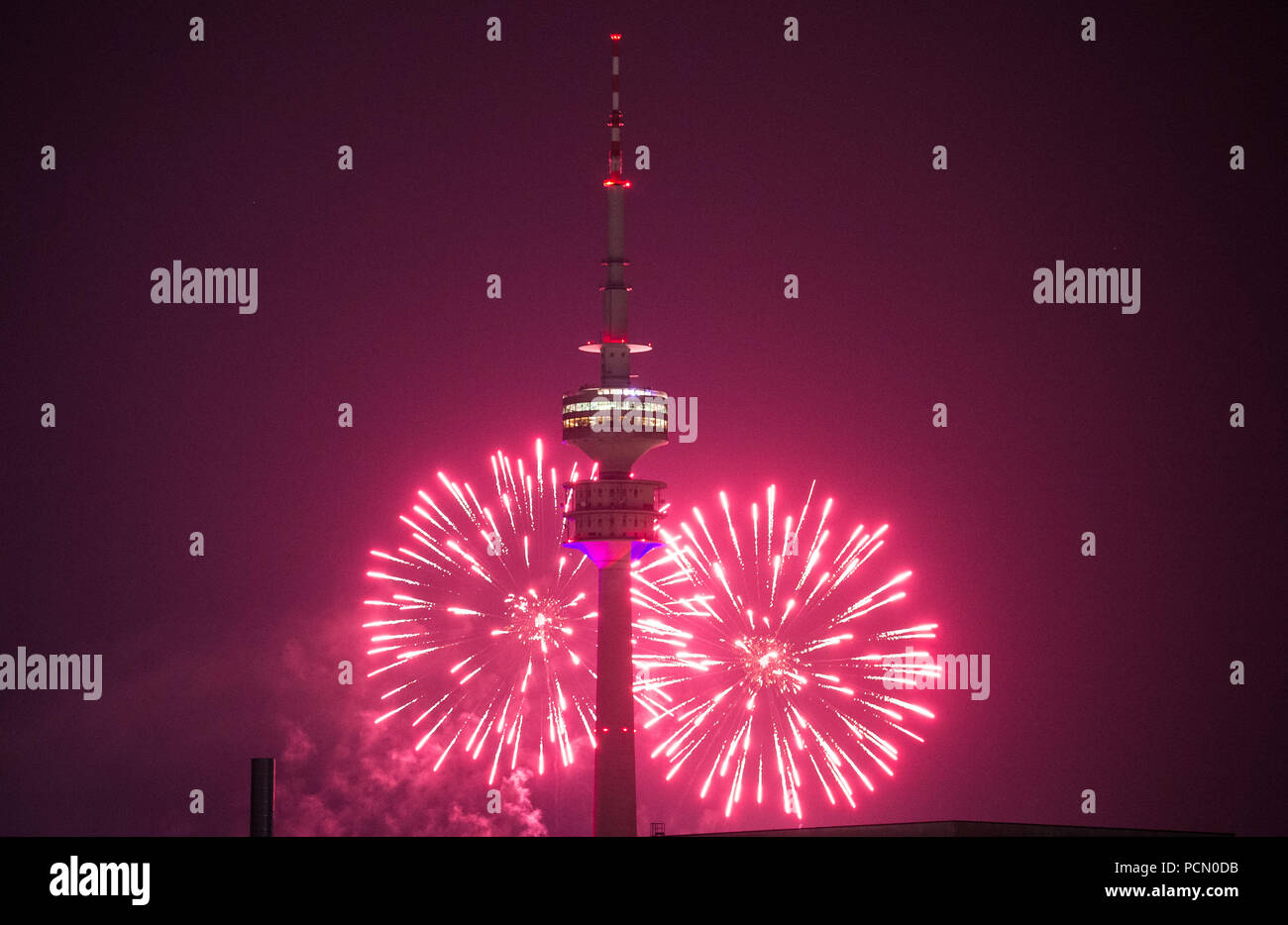 02. August 2018, München: Der Himmel hinter dem Olympic Tower ist hell erleuchtet von Feuerwerk in einem rosa Farbton. Das Feuerwerk war leuchtet während der Impark Sommerfest bei den Olympischen Park. Foto: Lino Mirgeler/dpa Stockfoto