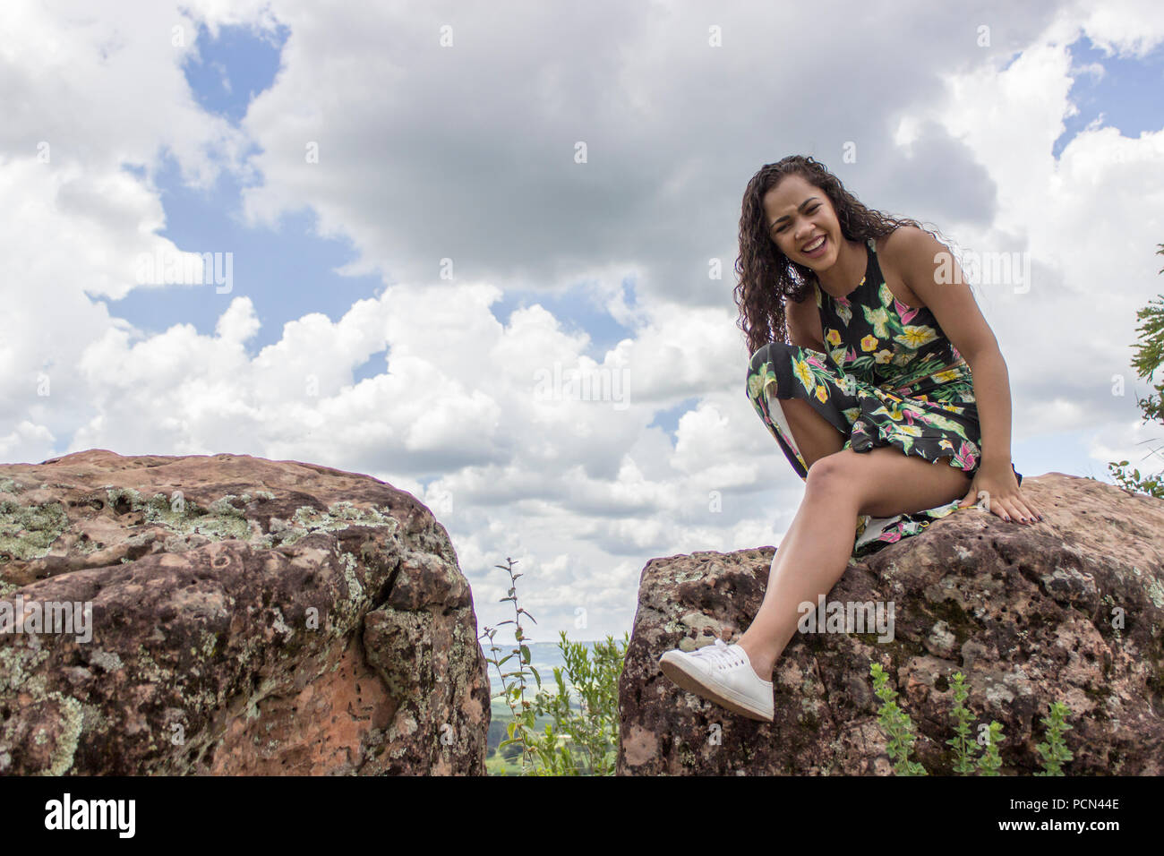 Schöne und lächelnd brünette Mädchen mit einem langen Kleid auf einem Stein auf einem Berg Stockfoto