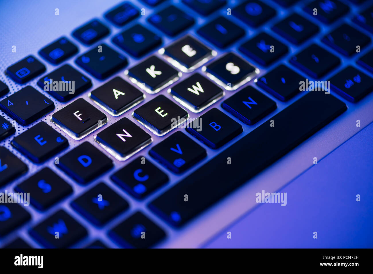 Gefälschte Nachrichten auf einem Laptop Tastatur mit Hintergrundbeleuchtung in der Nähe geschrieben mit selektiven Fokus in einem blauen Umgebungshelligkeit Stockfoto