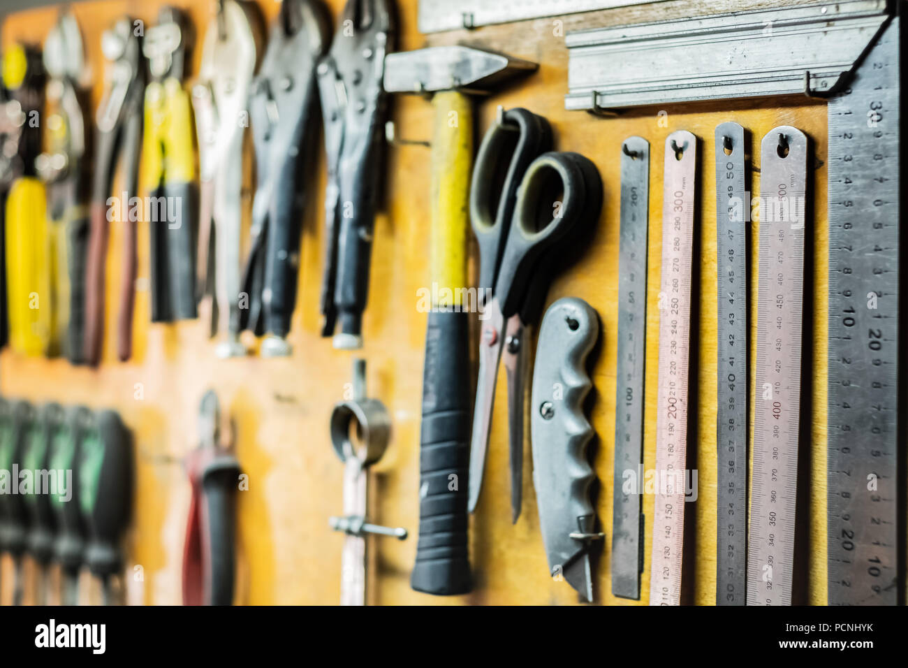 Werkzeuge und Geräte hängen an Werkstatt Wand. Lineale, Messer, Schere und andere Objekte im Arbeitsbereich angeordnet. Stockfoto