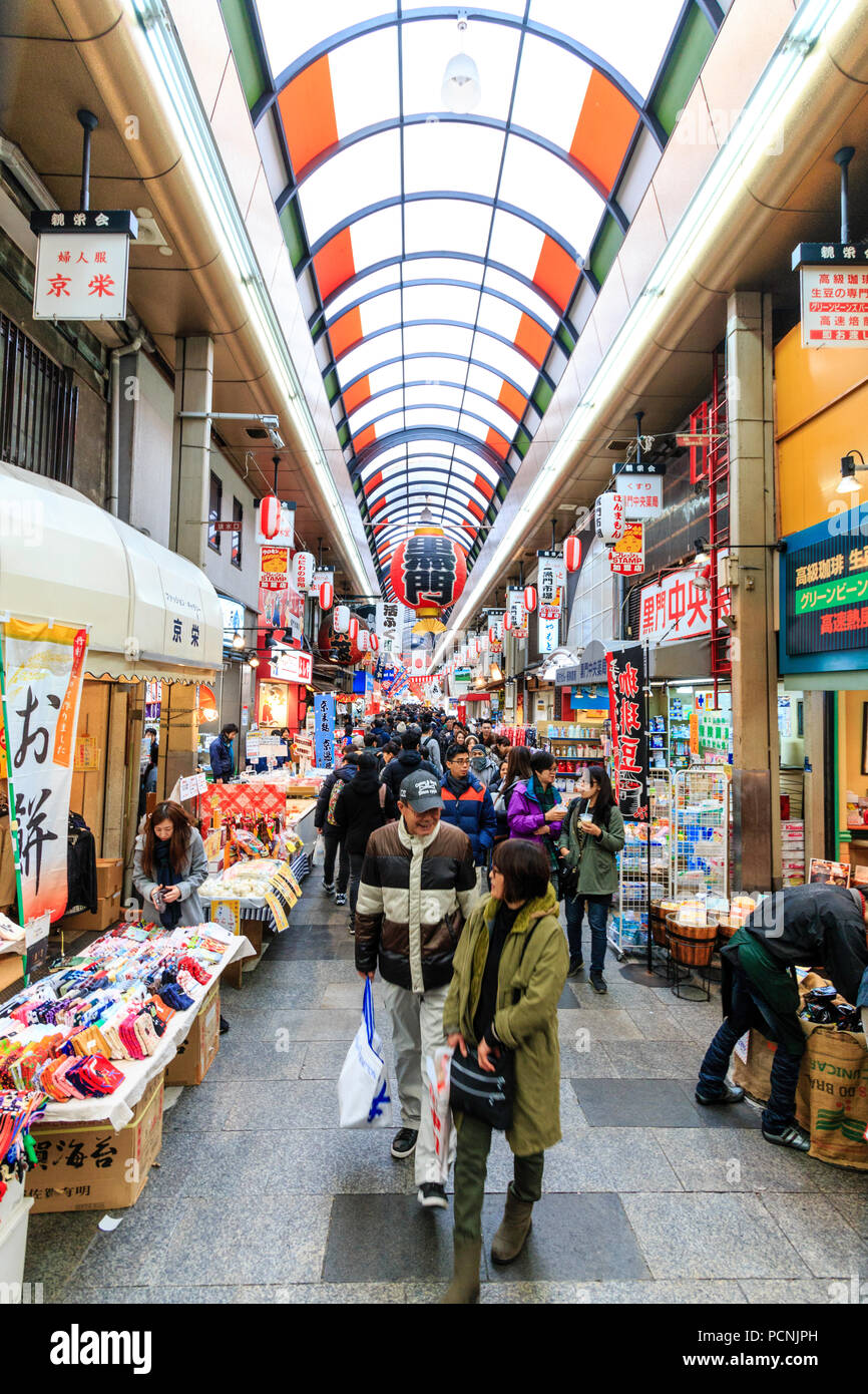 : Kuromon Ichiba, Küche essen Osaka's Markt. Blick entlang Arcade mit Ständen und Geschäften auf beiden Seiten. Besetzt mit Menschen überfüllt. Winter. Hohe Betrachtungswinkel Stockfoto