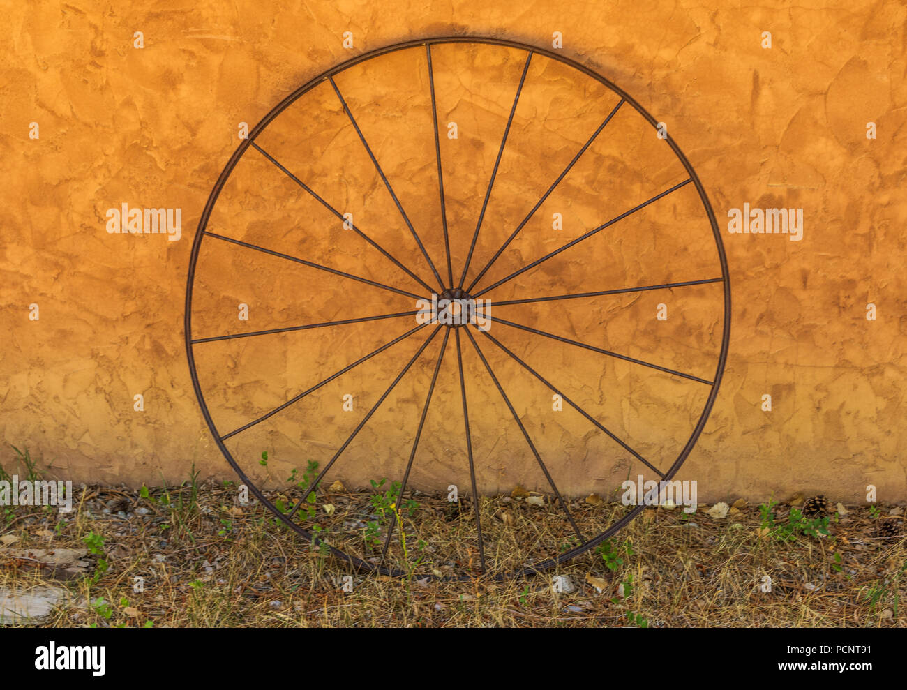 TAOS, NM, USA-8 Juli 18: eine einzige, einfache 16-Speichen wagen Bügeleisen wagon wheel gegen eine orange Stuck an der Wand lehnt. Stockfoto