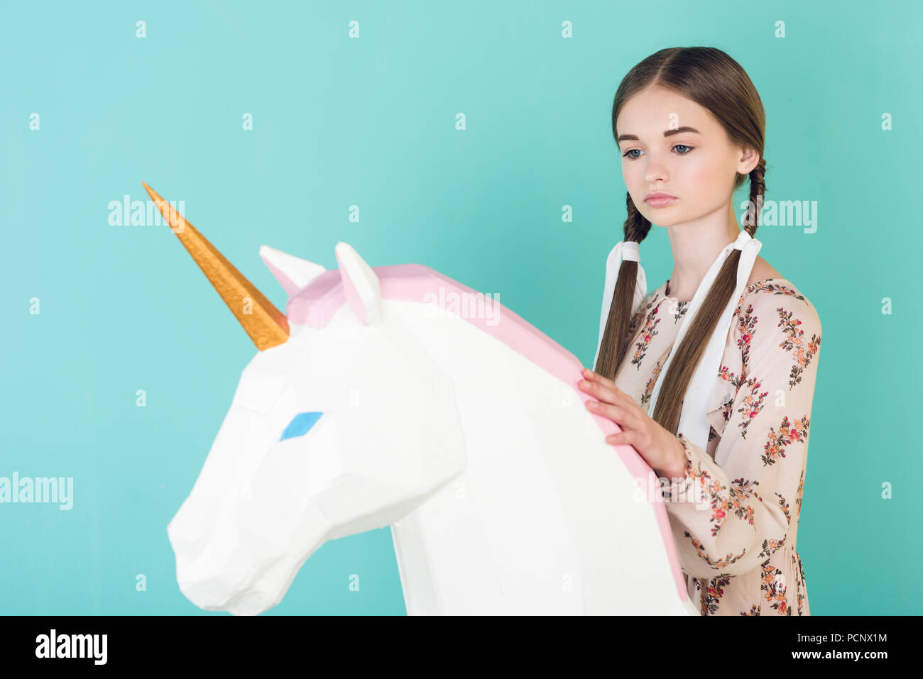 Stilvoll jugendlich Mädchen mit grossen toy Einhorn posiert, isoliert auf Türkis Stockfoto