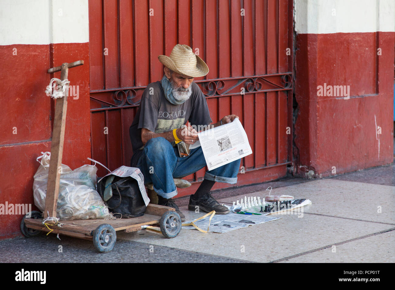 Karibik, Kuba, Havanna, älterer Mann mit Hut lesen beim Sitzen auf dem Bürgersteig Stockfoto