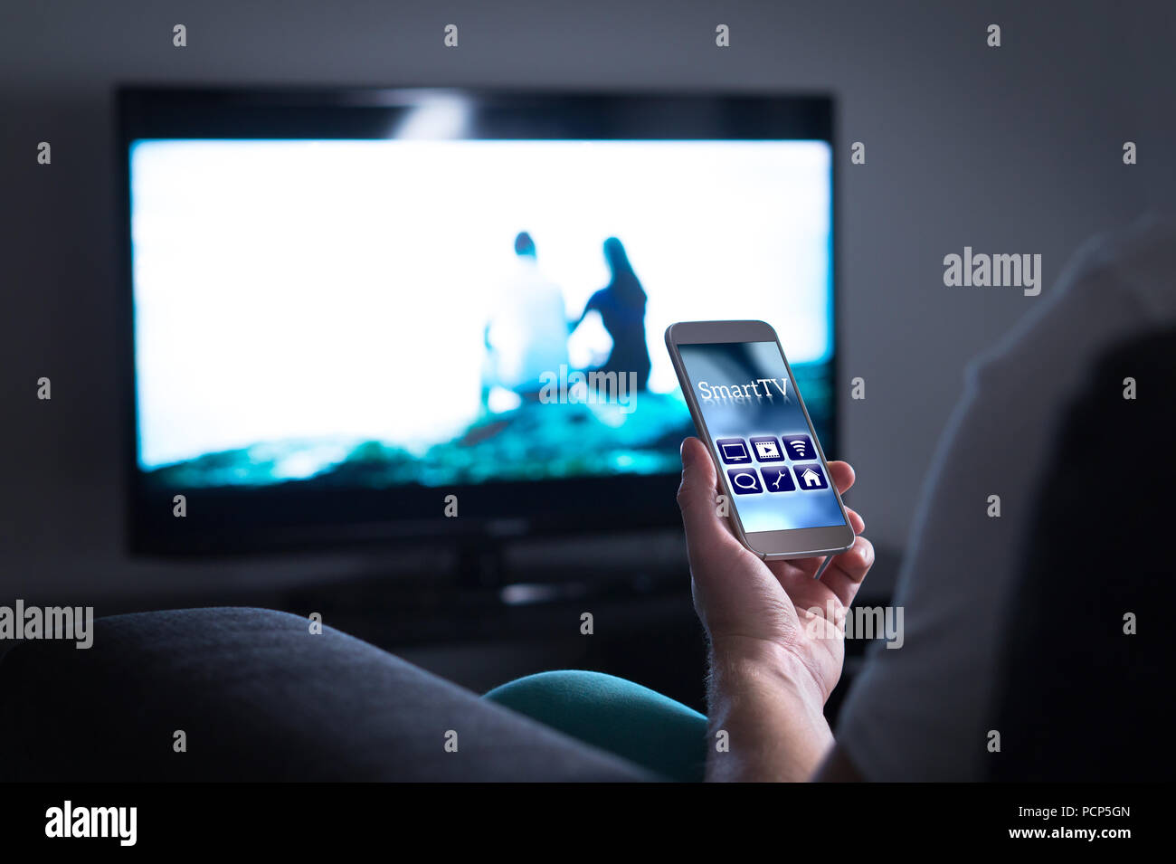 Man Fernsehen und mit Smart TV-Fernbedienung Anwendung auf Handy. Auswahl Film streamen, schaltkanal oder die Einstellungen ändern. Stockfoto