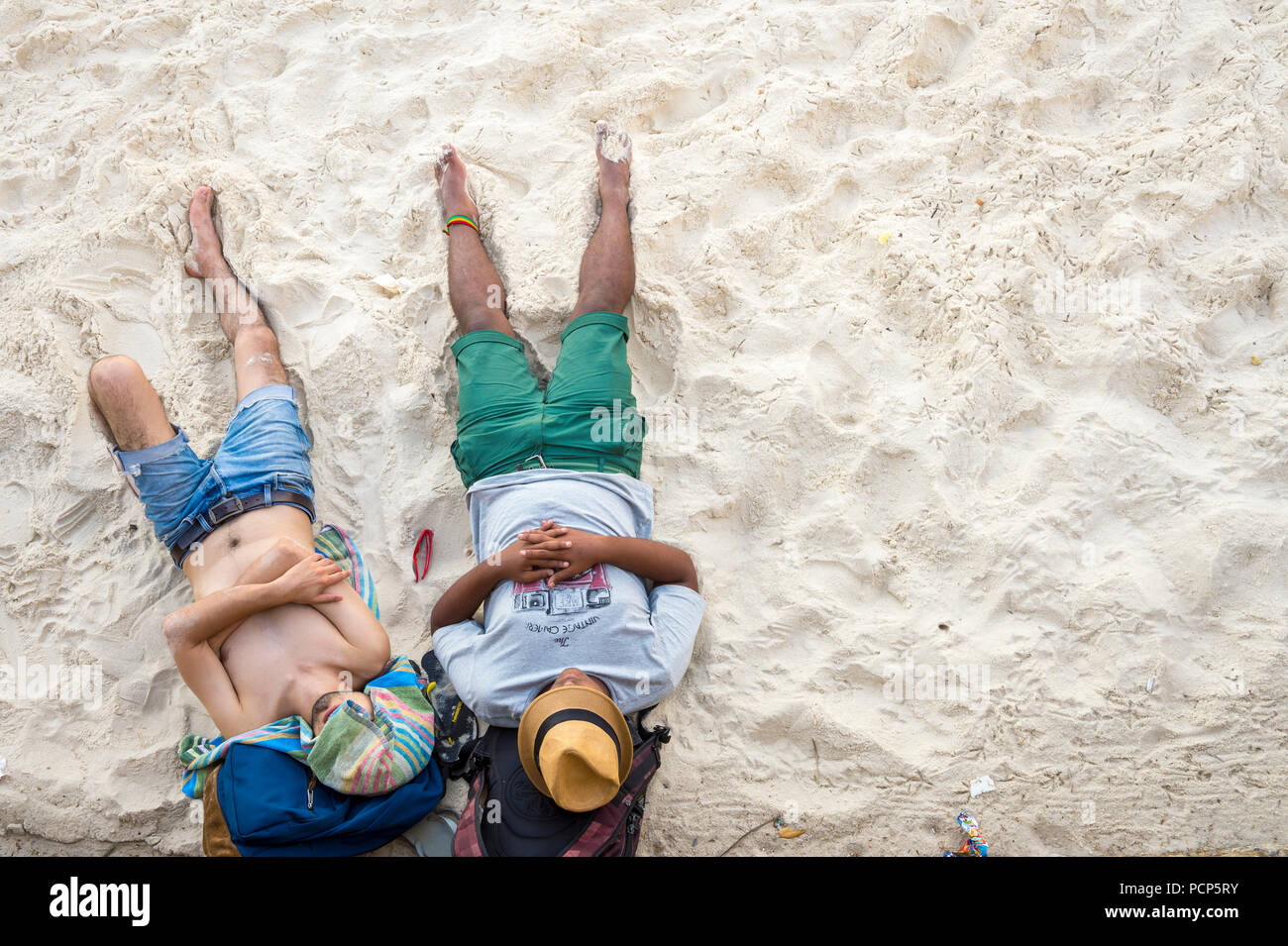 RIO DE JANEIRO - ca. Januar, 2014: Zwei junge Männer legen erschöpft und verkatert am Strand am Morgen nach einer Nacht Party. Stockfoto