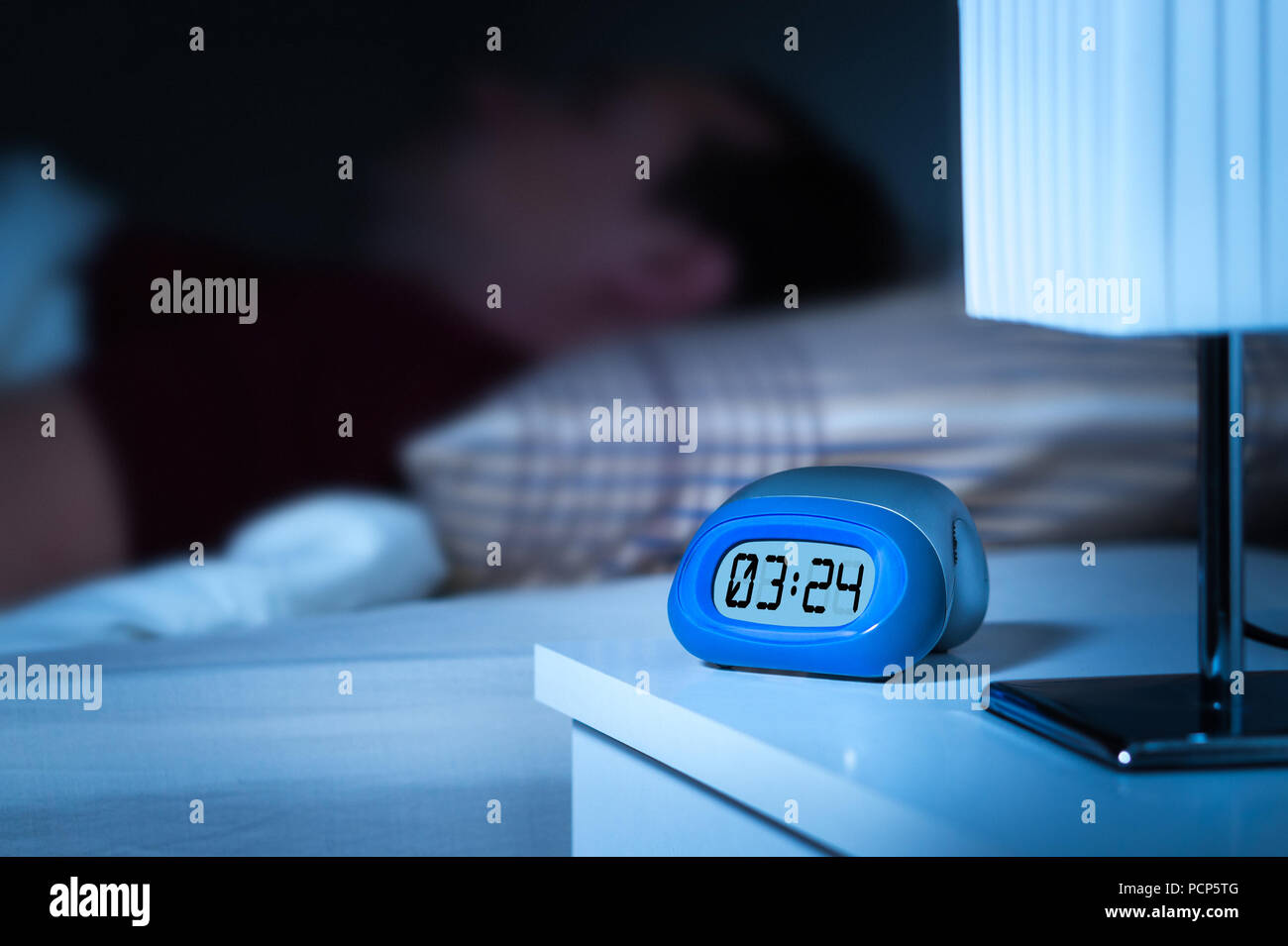 Schließen Sie bis zu digitaler Wecker auf dem Nachttisch im Schlafzimmer. Mann schlafen im Bett in den Hintergrund. Verträumt blur Effekt. Stockfoto