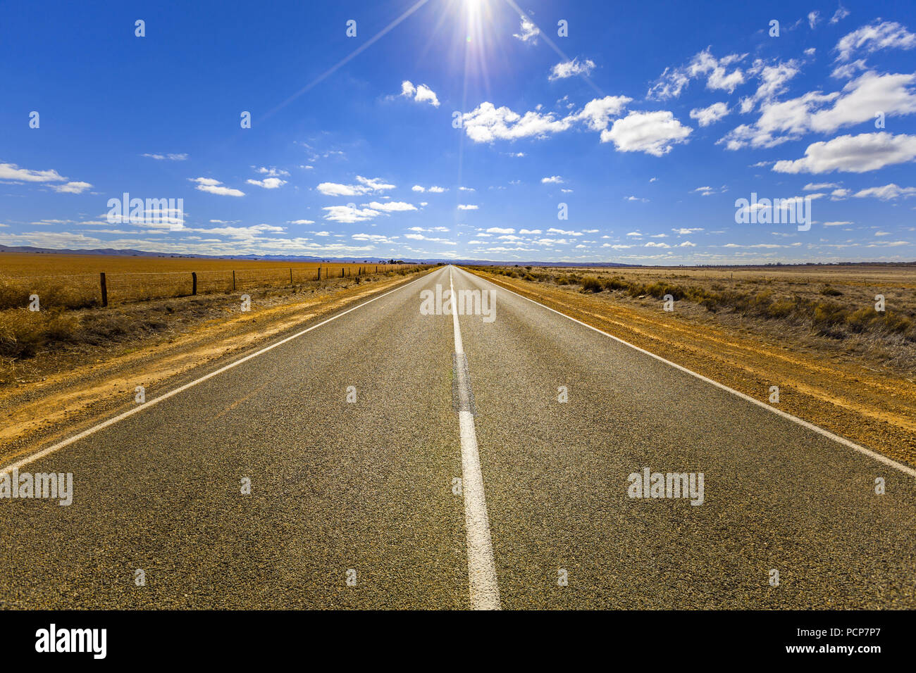 Landstraße, die durch landwirtschaftliche Felder auf hellen, sonnigen Tag mit Sonne flare Stockfoto