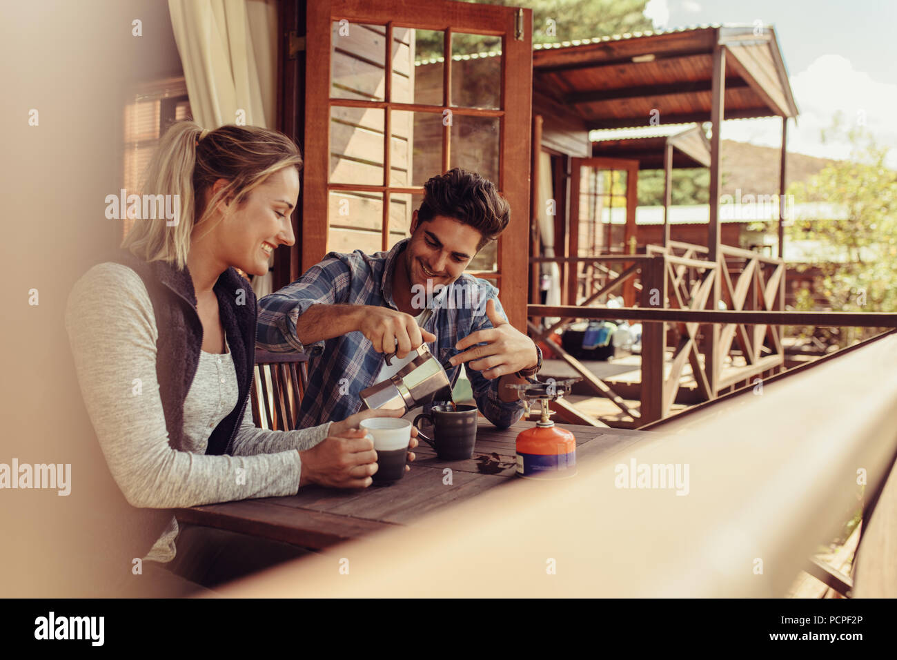 Paar außerhalb einer Ferienhütte und Kaffee sitzen. Mann Kaffee gießen in Schale mit seiner Freundin durch Sitzen. Stockfoto