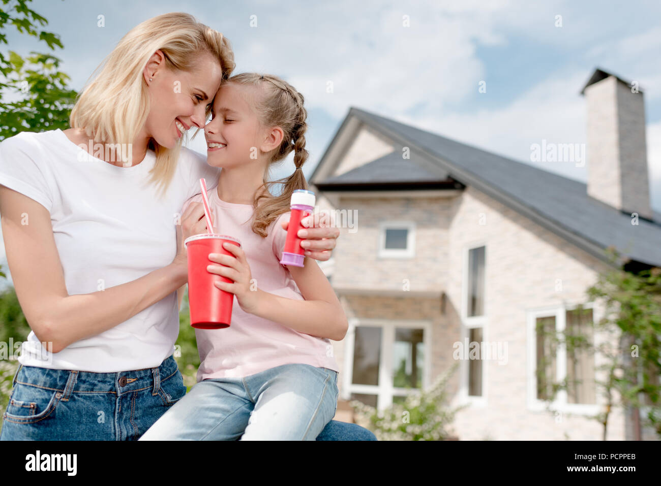 Gerne Frau sitzt Stirn an Stirn mit Tochter und Holding bubble Blower vor neues Haus Stockfoto