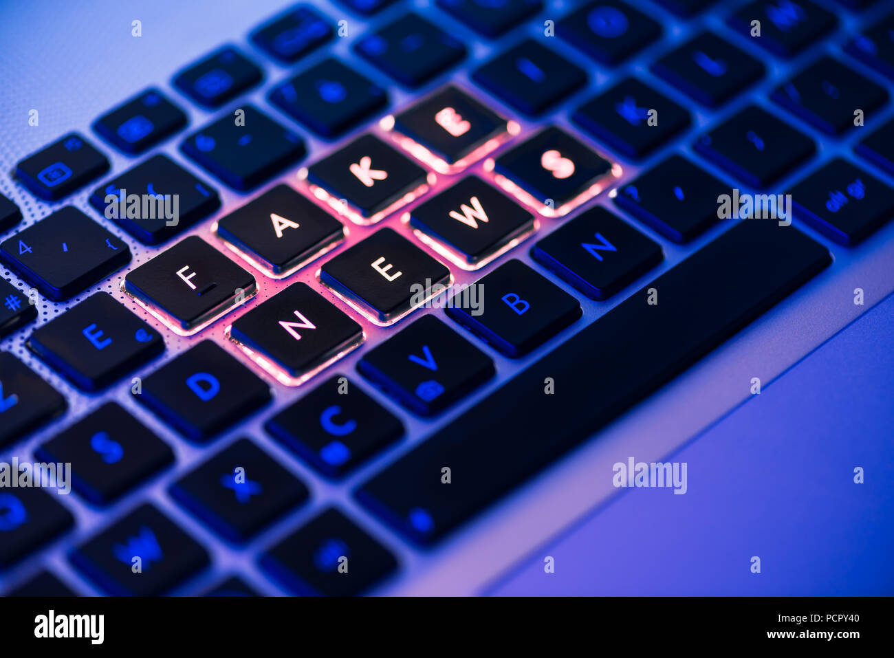 Gefälschte Nachrichten in Rot geschrieben auf einem Laptop Tastatur mit Hintergrundbeleuchtung close-up mit selektiven Fokus in einem blauen Umgebungshelligkeit Stockfoto