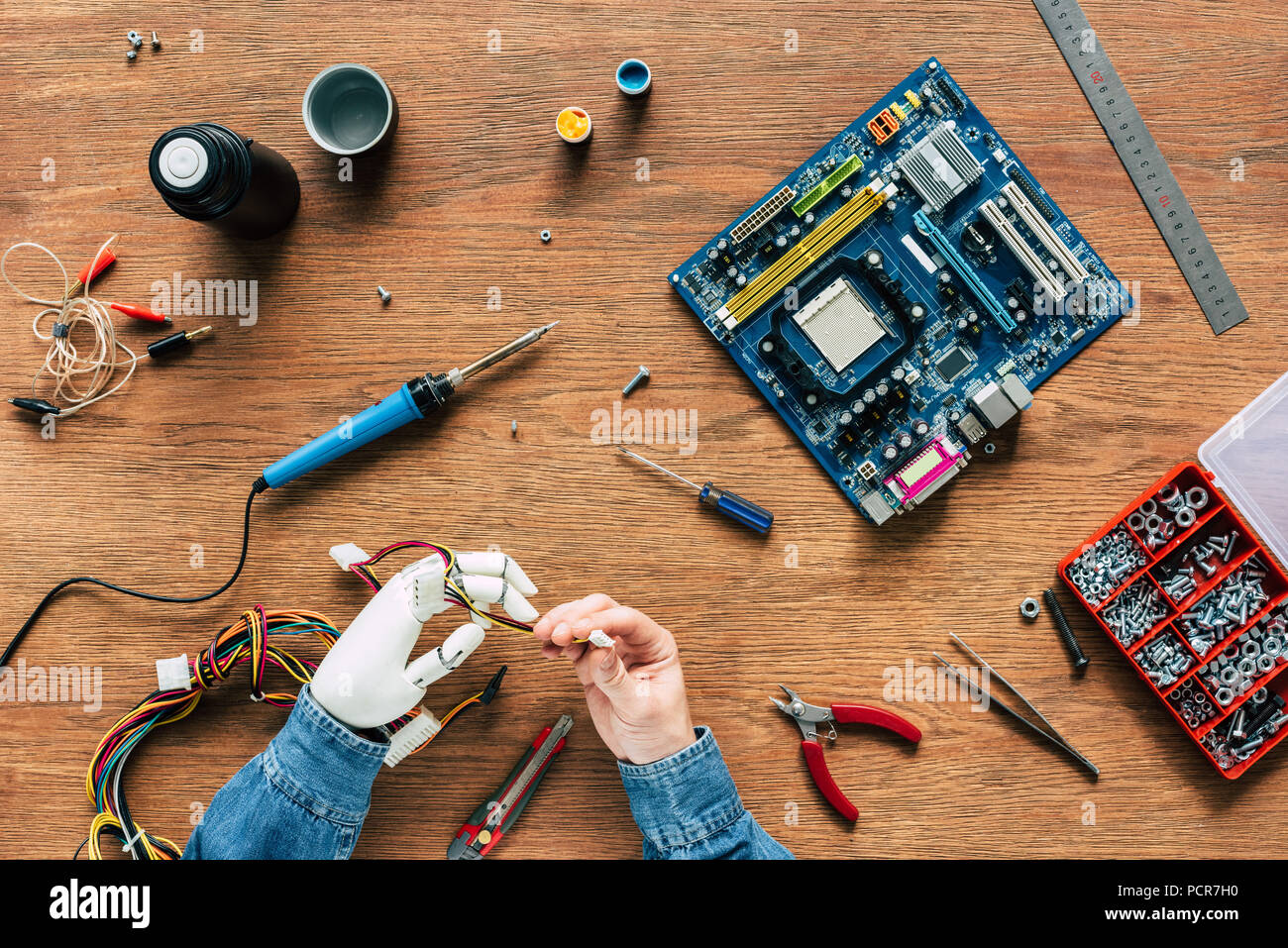 Zugeschnittenes Bild des Menschen mit roboterhand Kabel Holding mit Werkzeugen an den hölzernen Tisch Stockfoto