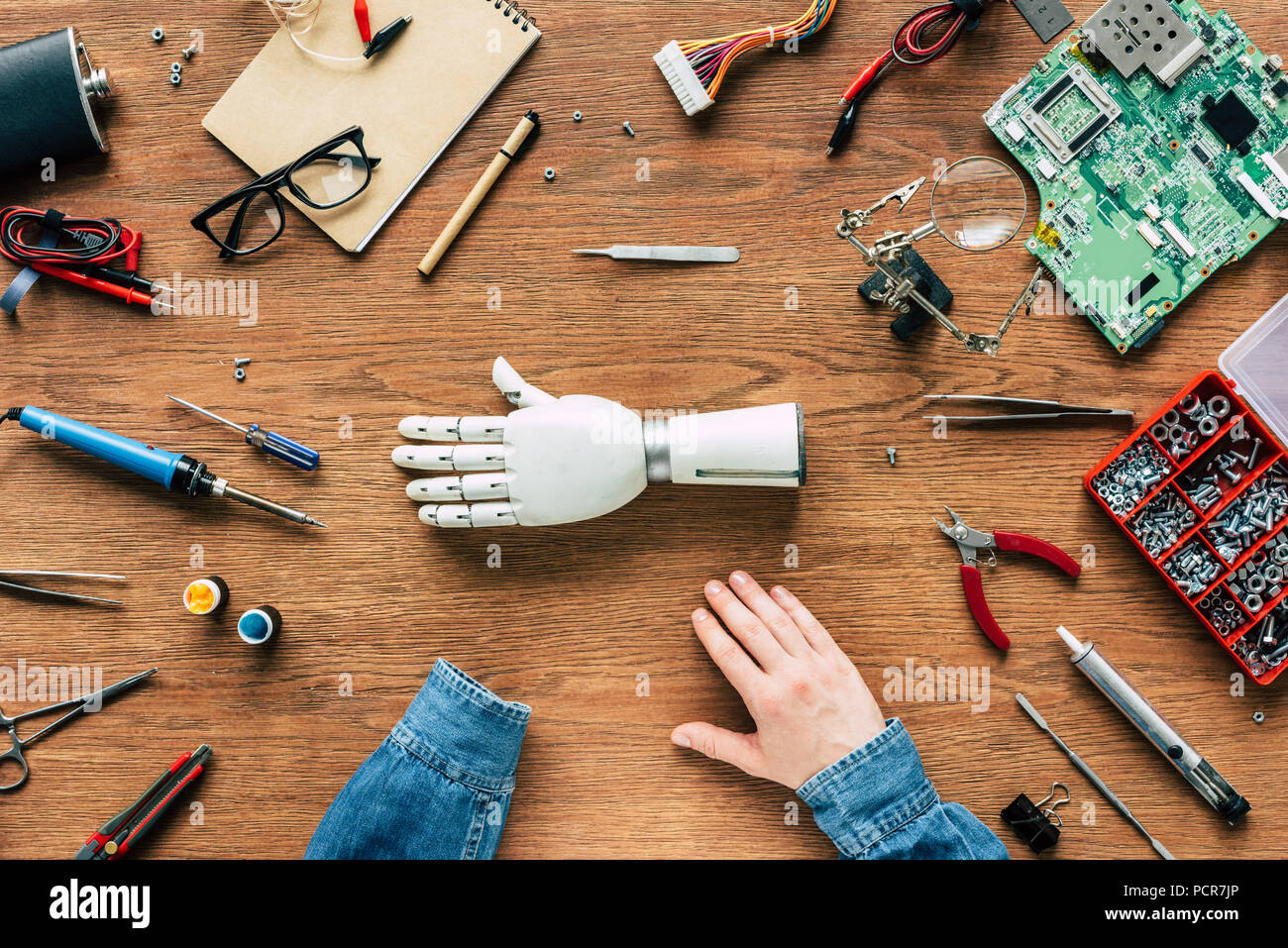 Zugeschnittenes Bild des Menschen mit amputierten am Tisch sitzen mit prothetischen Arm durch Tools umgeben Stockfoto