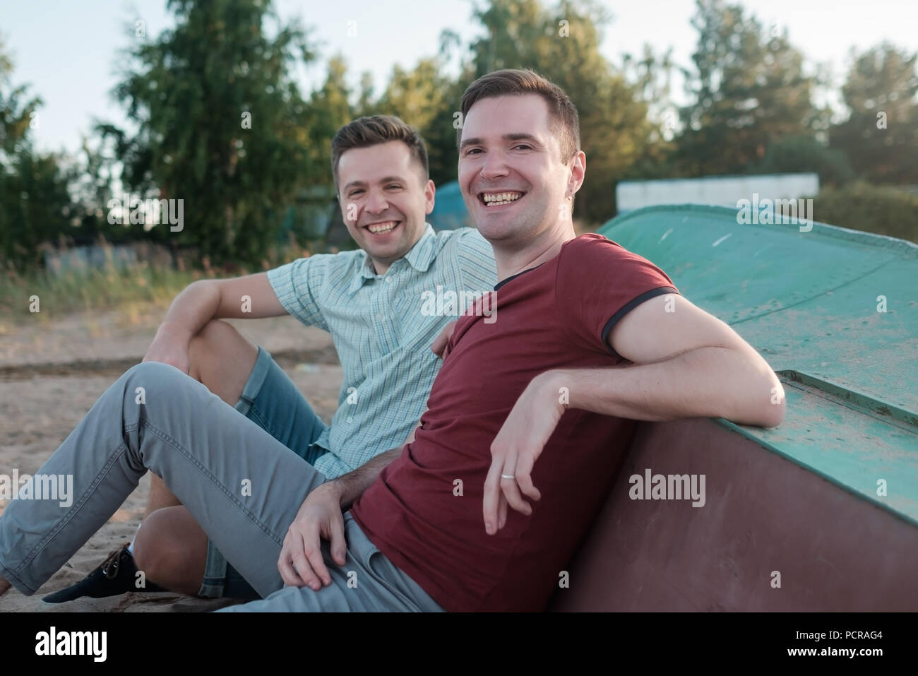 Zwei jungen kaukasischen Männern sitzen auf Sandstrand und lächelnd. Die besten Freunde von der Hochschule Konzept. Stockfoto