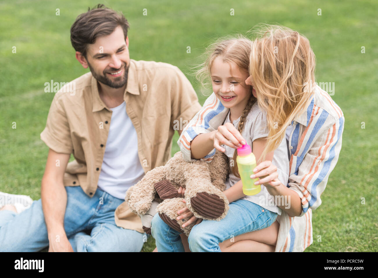 Hohe Betrachtungswinkel der glücklichen Familie mit einem Kind bläst Seifenblasen in Park Stockfoto