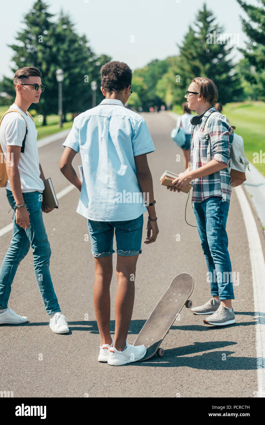 Multiethnischen Jungs im Teenageralter mit Bücher- und Skateboard stehen und sprechen in Park Stockfoto