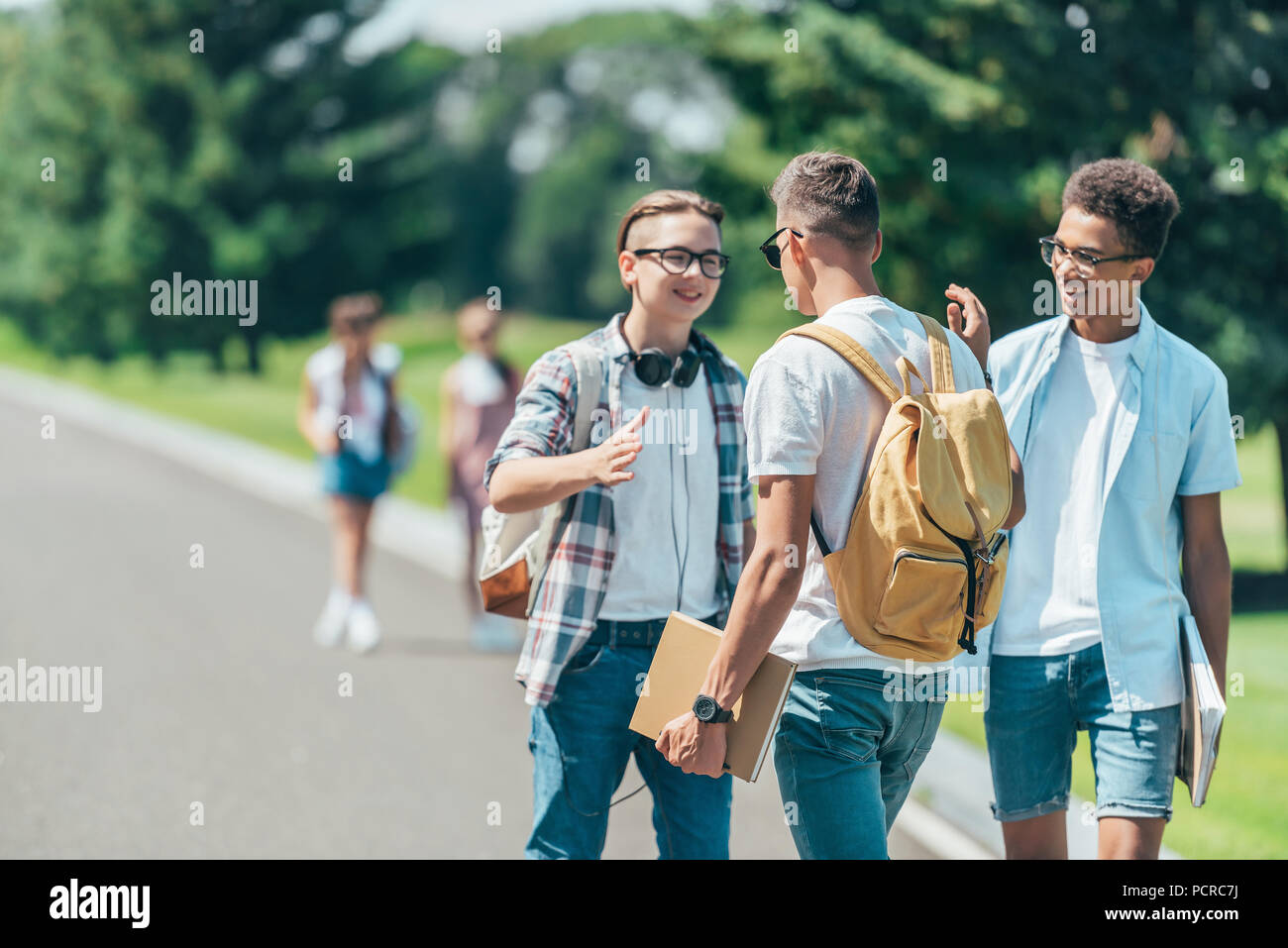 Multiethnischen Jungs im Teenageralter mit Büchern und Rucksäcke reden und lächeln einander in Park Stockfoto