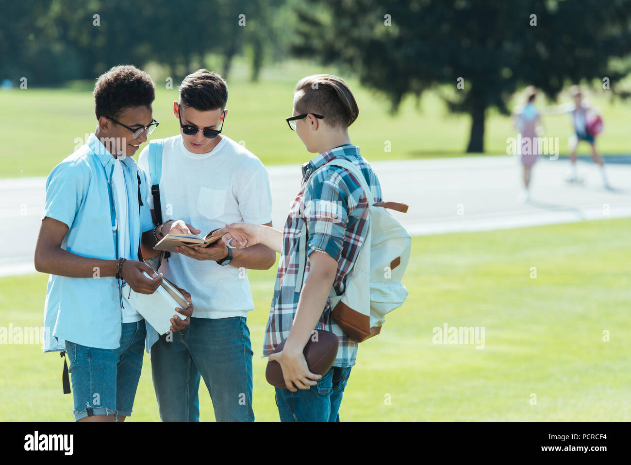 Multiethnischen Jungs im Teenageralter mit Büchern und Rucksäcke stehen und gemeinsam im Gespräch in Park Stockfoto