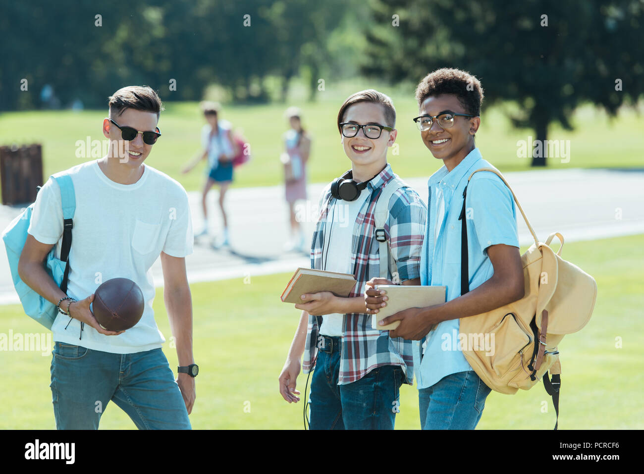 Multiethnischen Jungs im Teenageralter mit Büchern und Rucksäcke lächelnd an Kamera im Park Stockfoto
