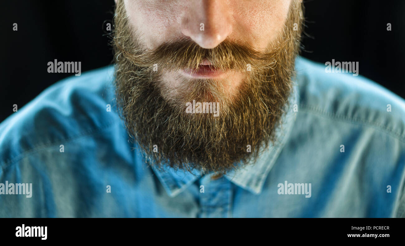 Attribute der Erscheinung einer Hipster Mann: Schnurrbart und Bart. Portrait von bärtigen Mann in ein blaues Jeanshemd auf schwarzem Hintergrund Stockfoto